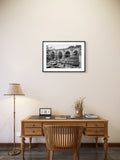 Wooden desk with chair, lamp, and framed picture on a beige wall.