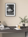 Framed black and white photograph of a building on a wall above a desk with decor items.