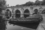 Boats docked at a lock on a canal with a stone bridge in the background