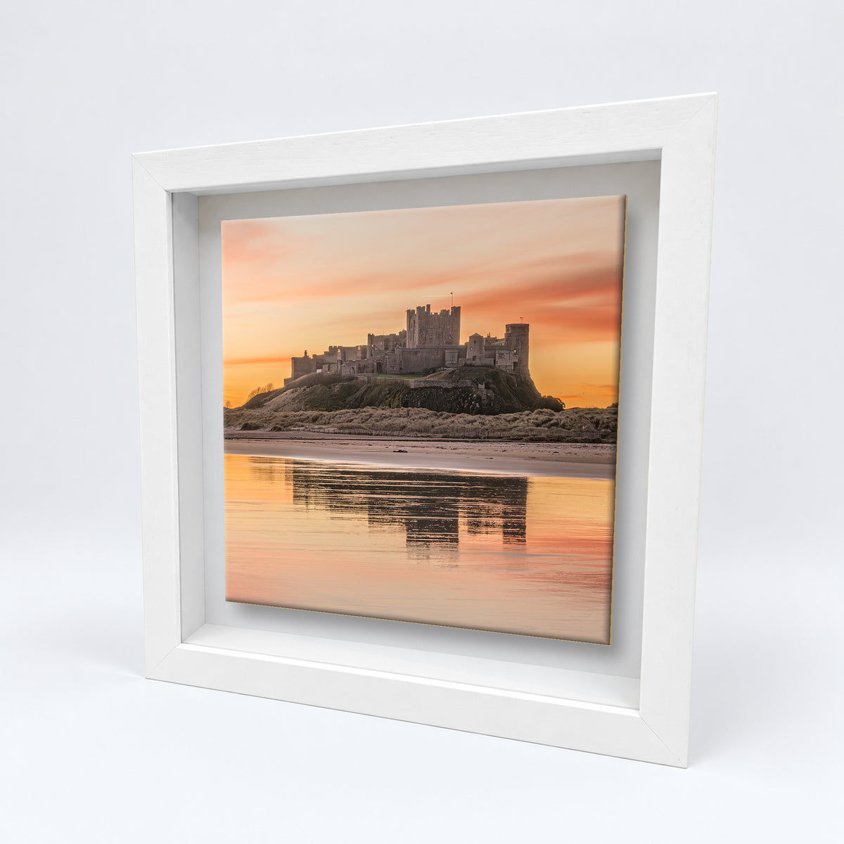 Bamburgh Castle at Sunrise on an 8×8 inch ceramic tile in a white box frame, angled view
