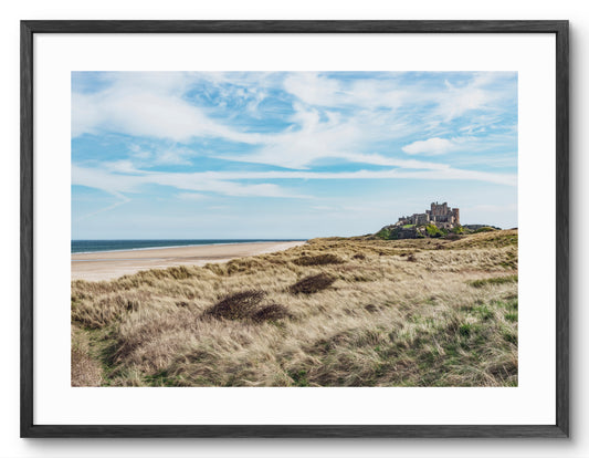 Bamburgh Castle beach and grass-covered dunes shown as a framed photographic print.