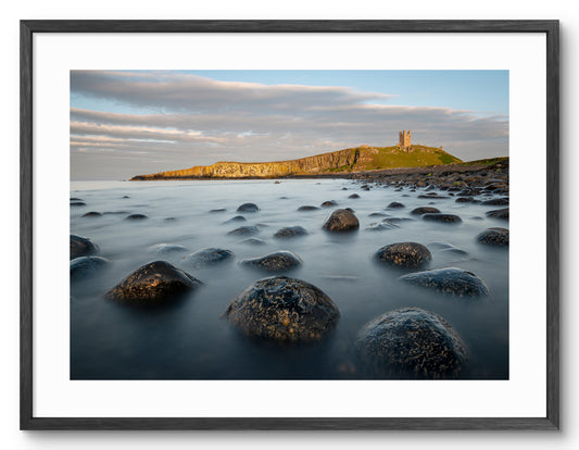 Boulder Beach and Dunstanburgh Castle at Embleton shown as a framed photographic print.