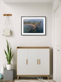 Framed artwork of a coastal scene above a white cabinet with wooden accents.