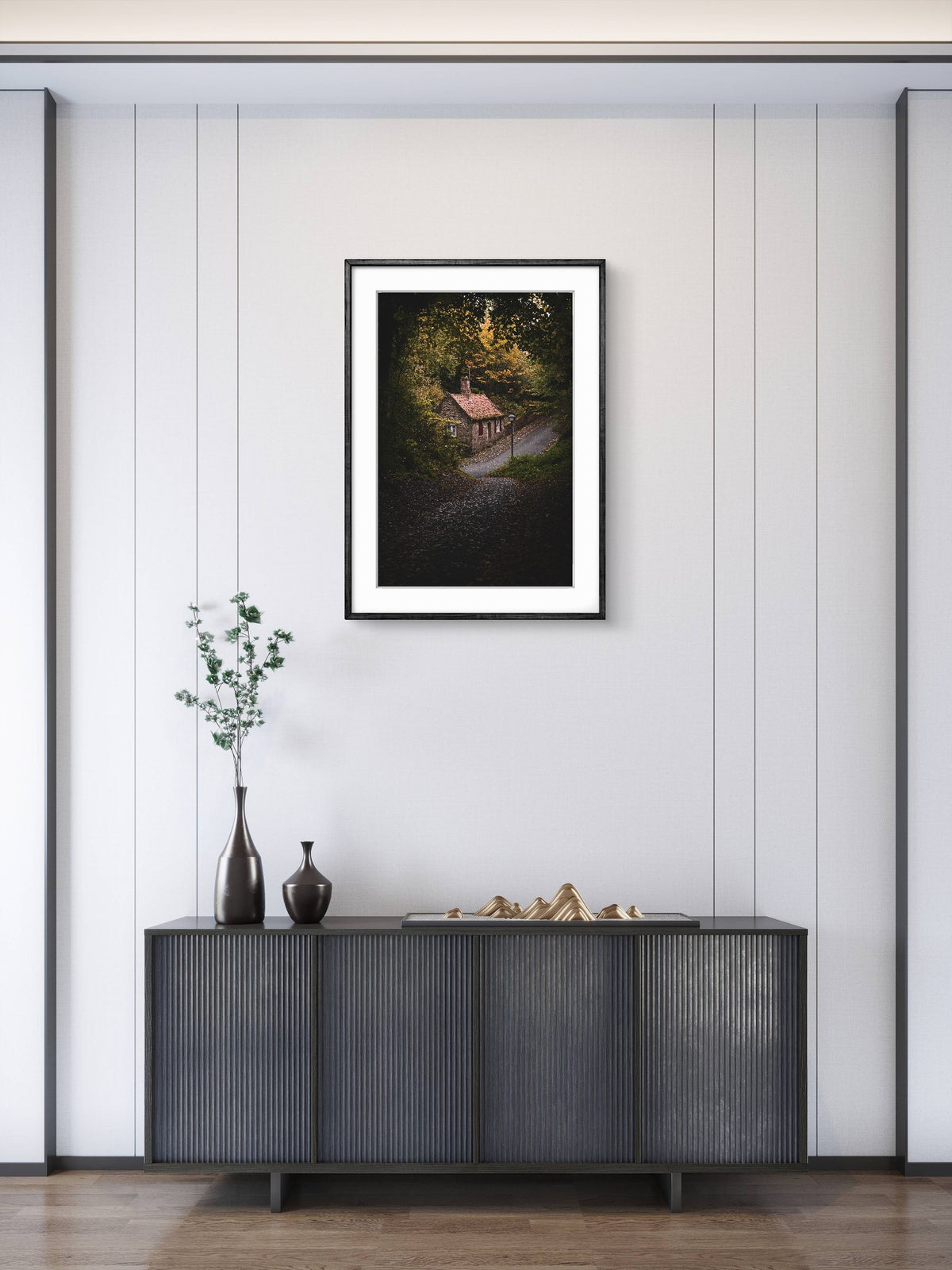 Framed artwork above a dark wooden cabinet with decorative items on a light gray wall.