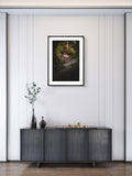 Framed artwork above a dark wooden cabinet with decorative items on a light gray wall.