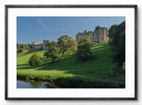 Castle on a hill with green trees and a river in the foreground, framed picture.