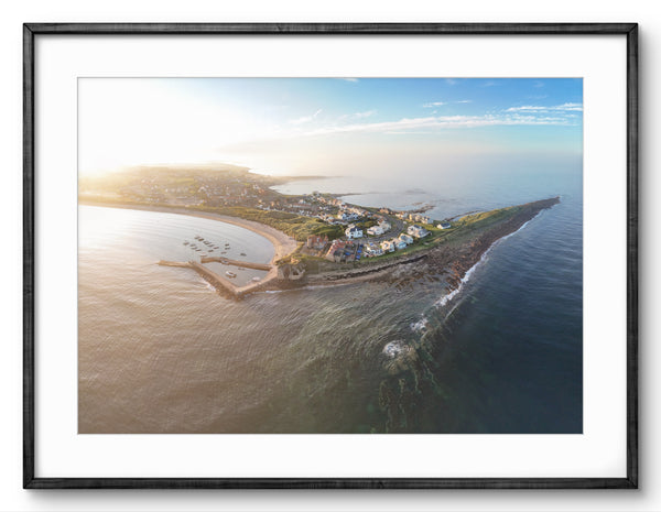 Aerial view of a coastal area with houses and a lighthouse, framed in black.