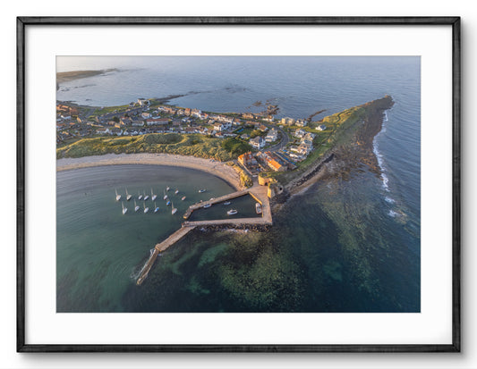 Aerial view of a coastal town with a pier and boats, framed in black.
