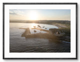 Framed photograph of a sunset over a dock with boats on a body of water.