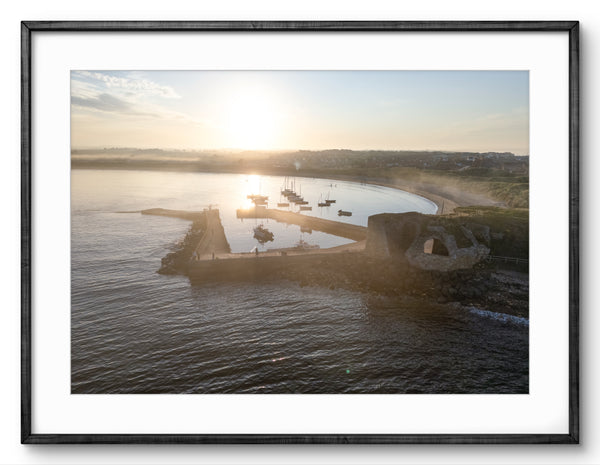 Framed photograph of a sunset over a dock with boats on a body of water.