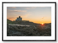 Lighthouse on a rocky cliff at sunset with a framed border