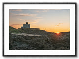 Lighthouse on a rocky cliff at sunset with a framed border