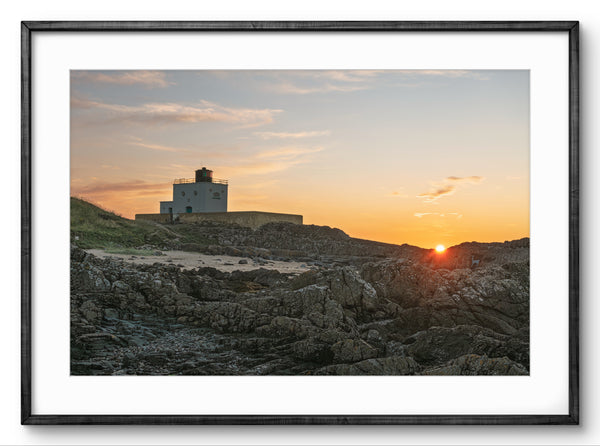 Lighthouse on a rocky cliff at sunset with a framed border