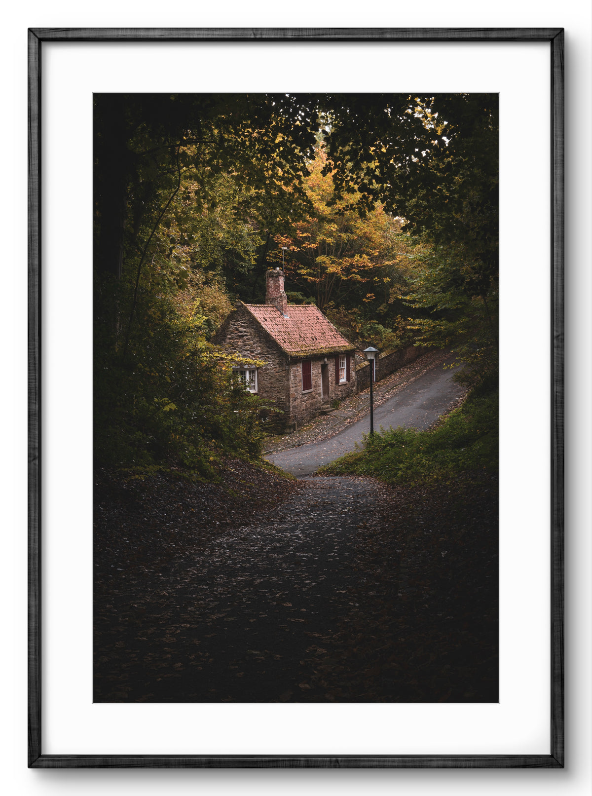 Framed artwork of a small house nestled among trees on a hillside.