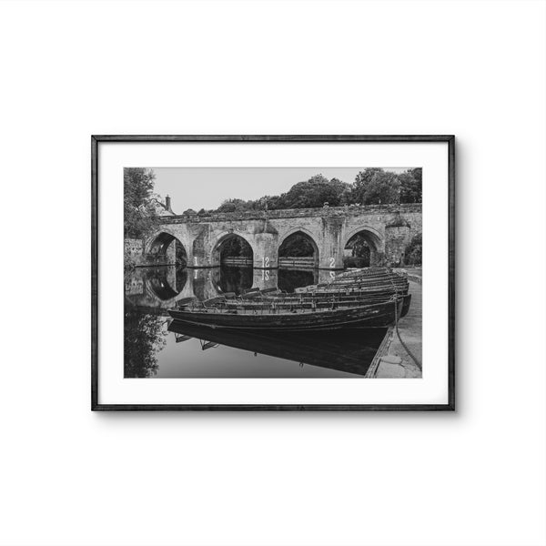 Framed black and white photograph of a boat on a river with a stone bridge in the background.