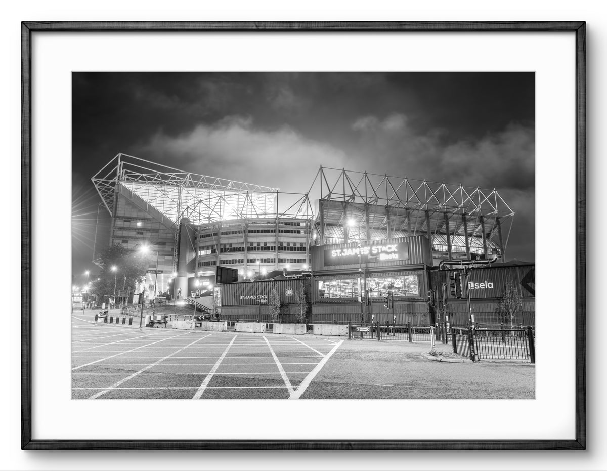 Black and white image of a stadium at night with illuminated signs.