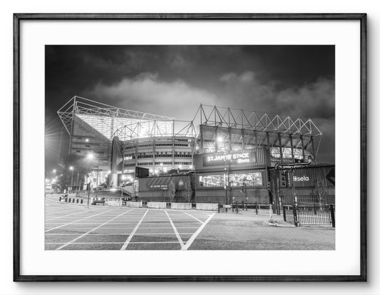 Black and white image of a stadium at night with illuminated signs.