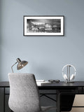Framed black and white photo above a desk with a chair and lamp in an office setting.