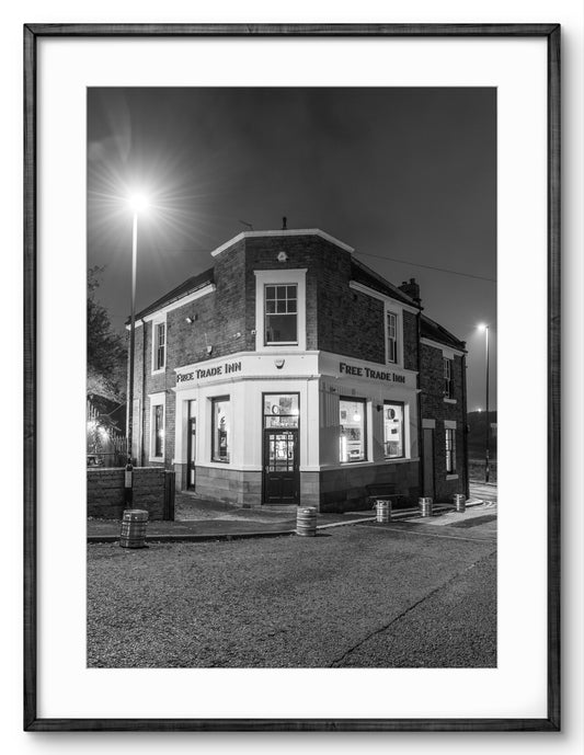 Black and white photograph of a pub at night with illuminated windows.