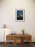Wooden desk with chair, lamp, and framed picture of a lighthouse on a wall.
