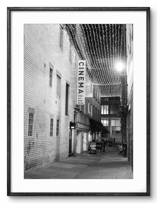 Framed black and white photo of a city street with a cinema sign.
