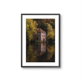 Framed photograph of a house by a lake with trees in the background