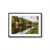 Framed photograph of a scenic lake with trees and a building.