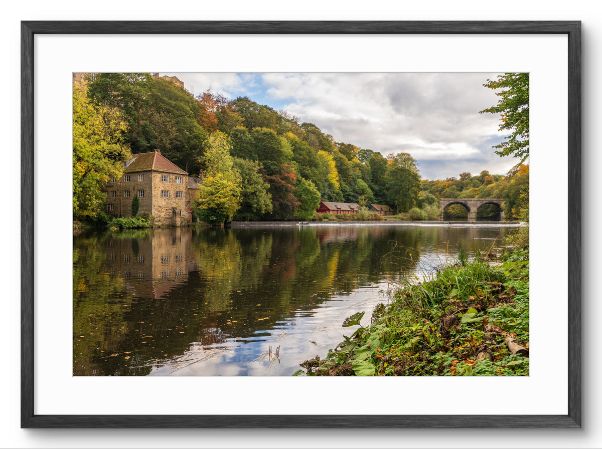 Framed photograph of a serene landscape with a river, bridge, and trees.