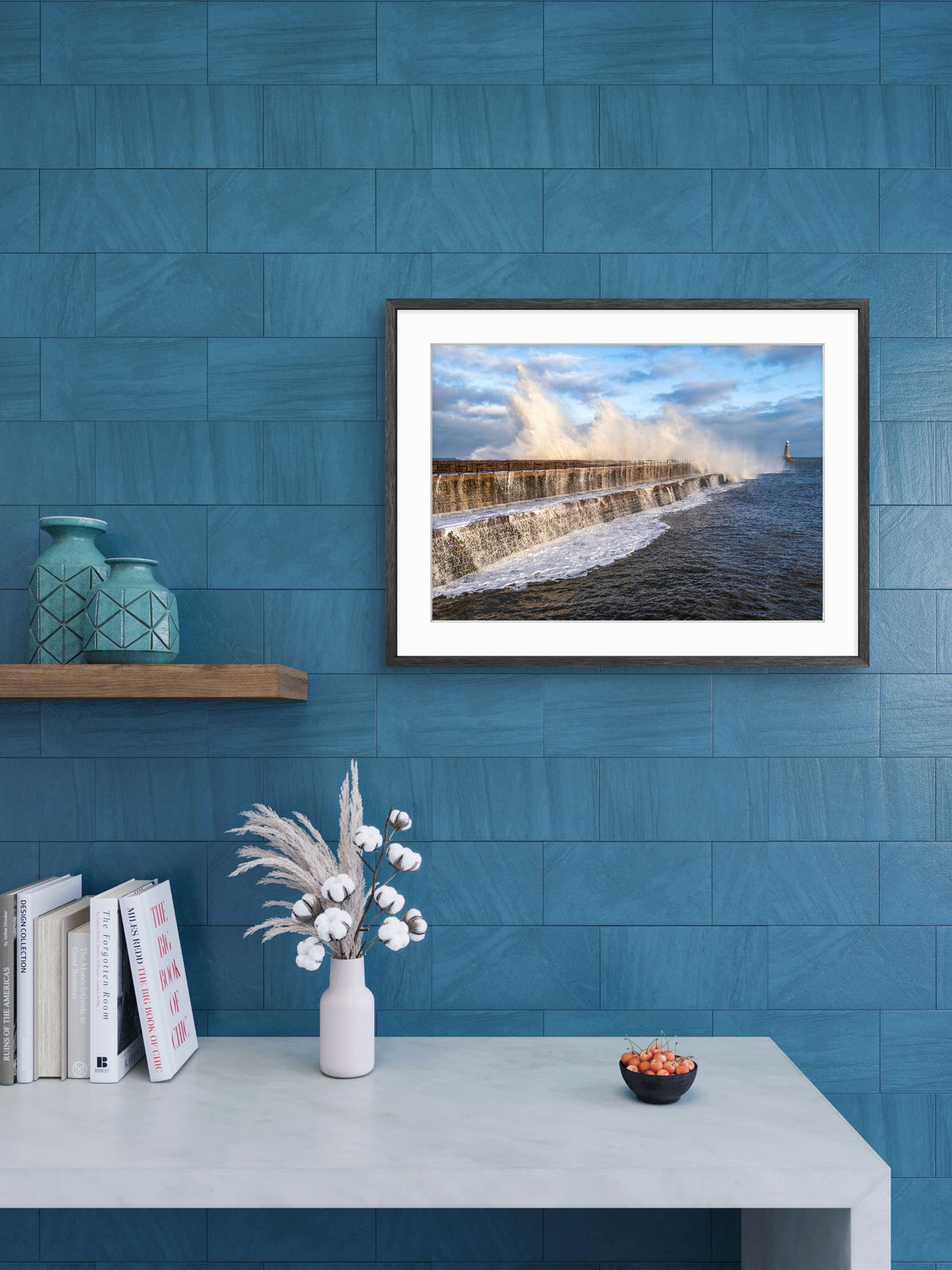 Framed artwork of a coastal scene on a blue wall with decorative items below.