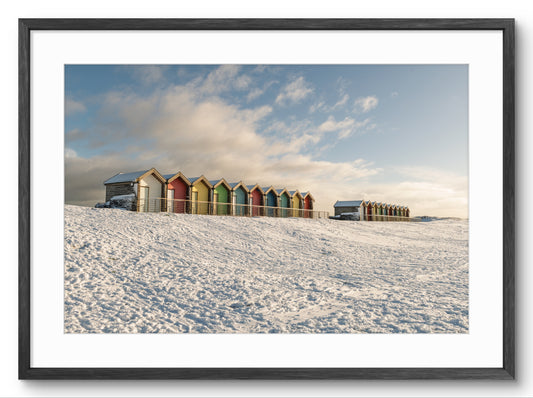 Colorful beach huts in a snowy landscape with a blue sky.