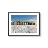Framed photograph of colorful beach huts in the snow against a blue sky.
