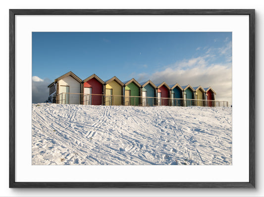 Colorful beach huts on a snowy landscape with a blue sky.