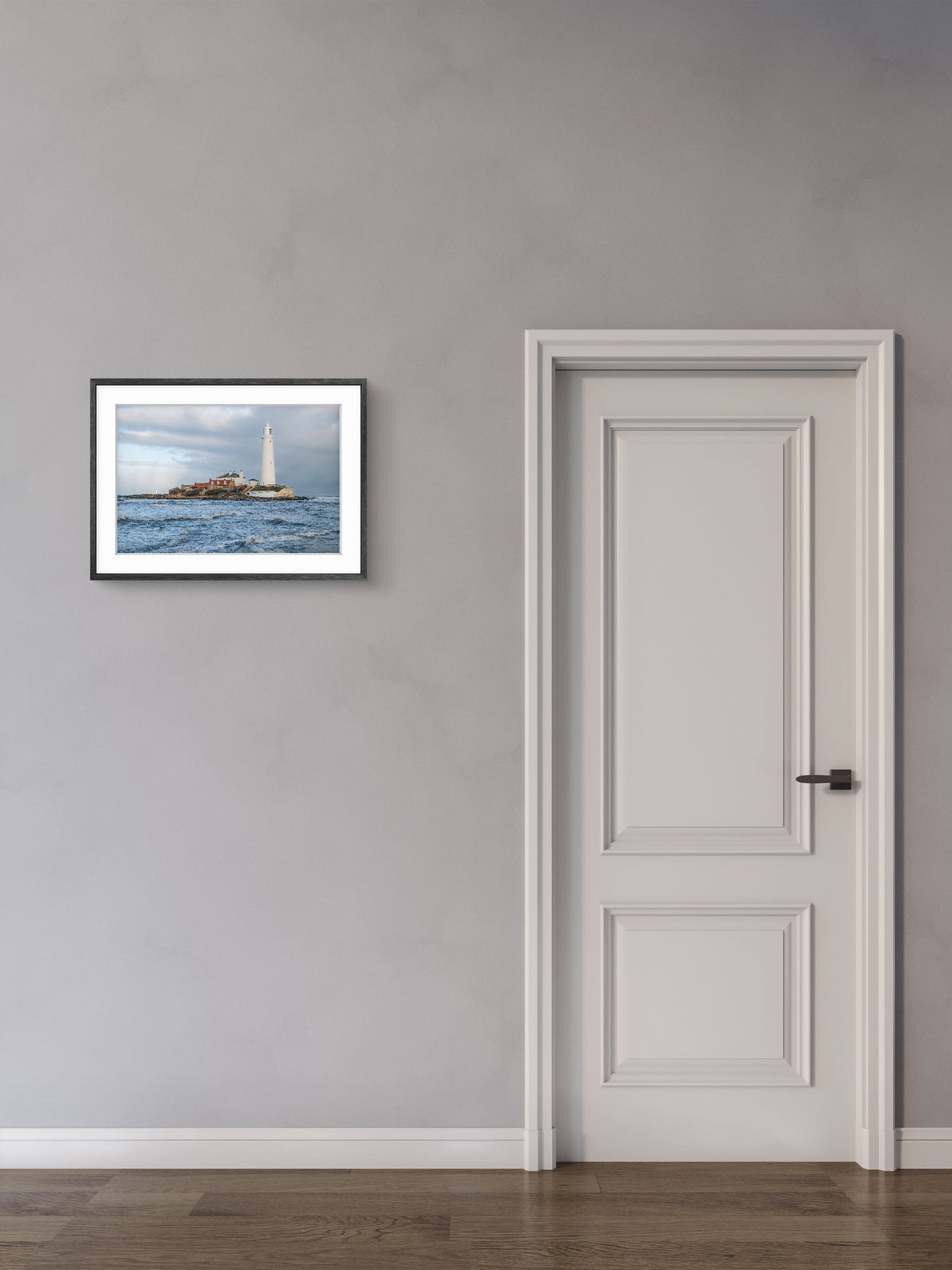 Framed artwork of a lighthouse on a gray wall next to a white door.
