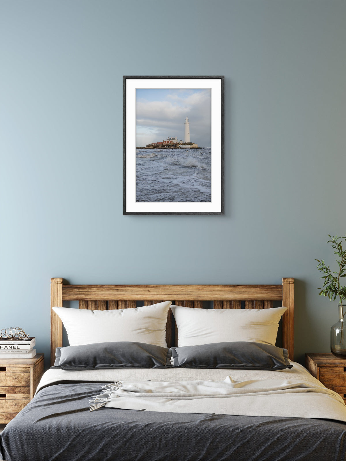 Framed artwork of a lighthouse over water above a bed in a bedroom.