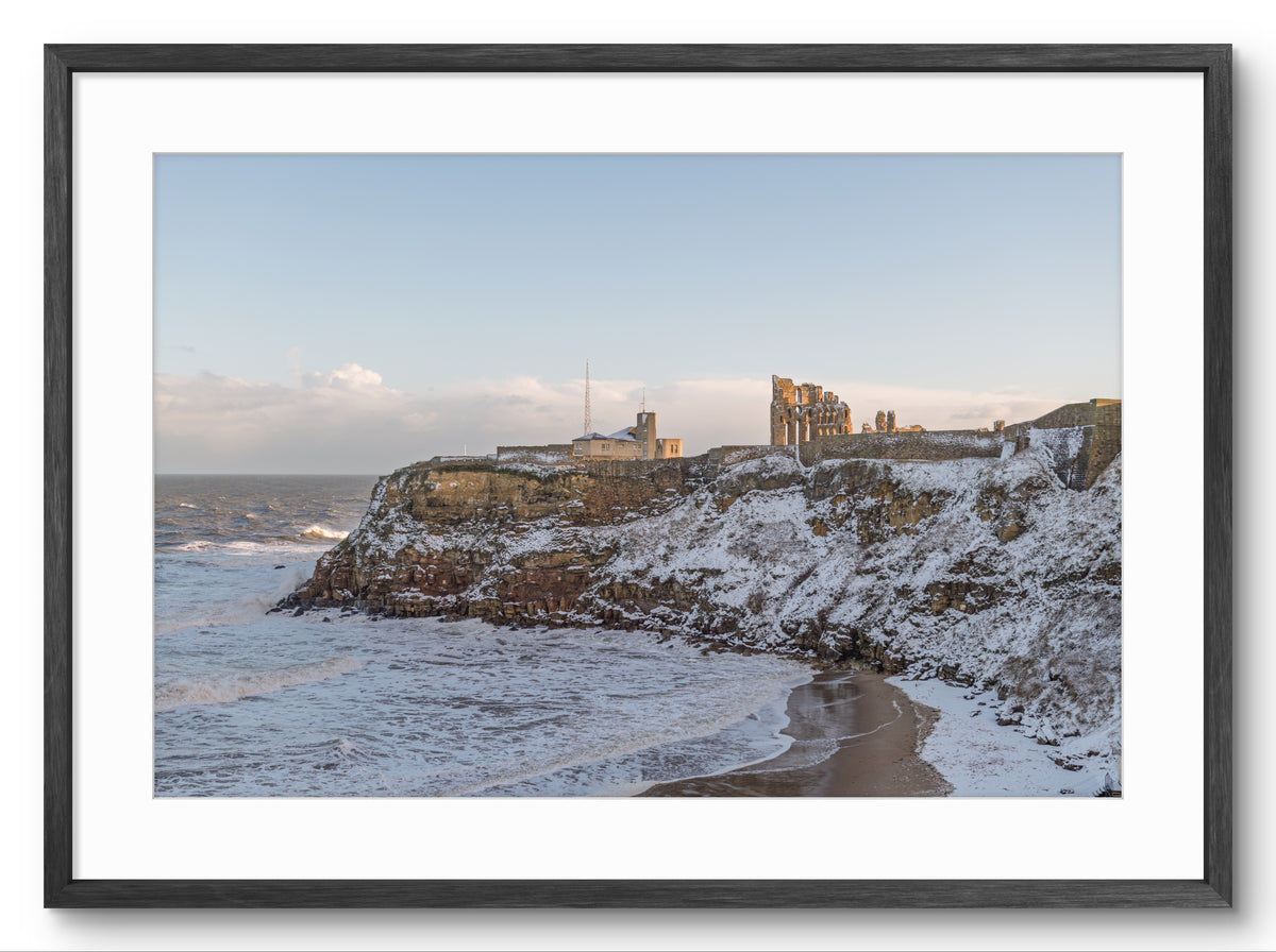 Framed photograph of a coastal scene with a castle on a cliff edge.