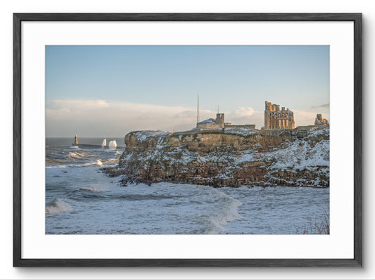 Framed photograph of a coastal scene with a castle on a cliff overlooking the sea.
