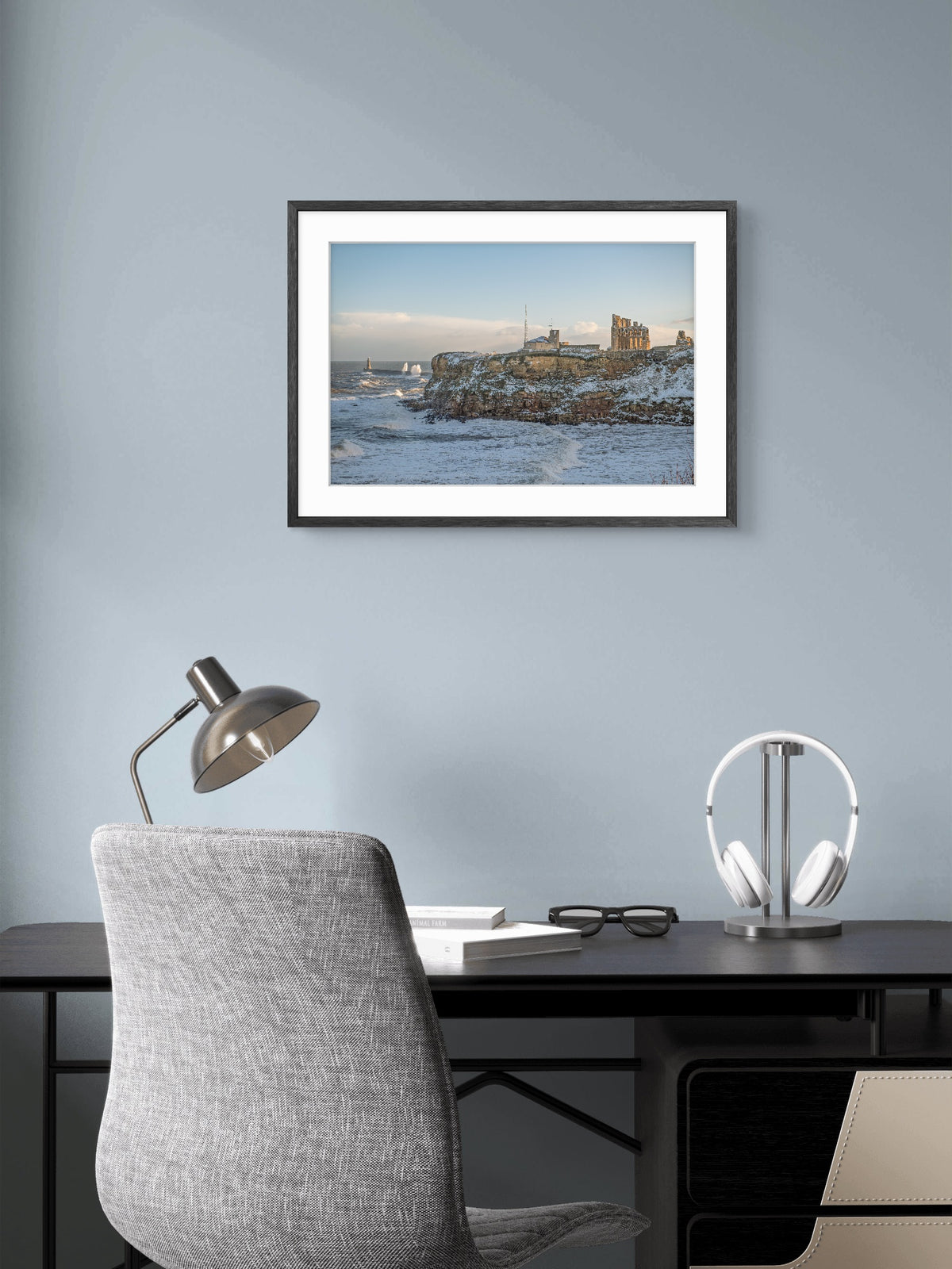 Framed artwork above a desk with a chair and lamp in an office setting.