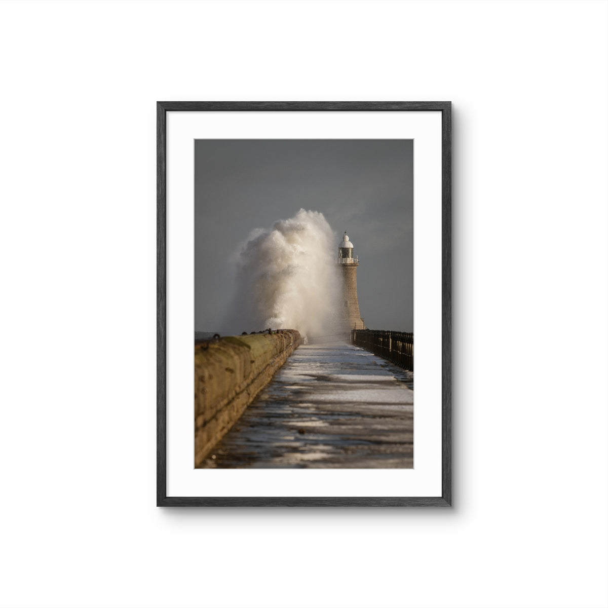 Framed photograph of a lighthouse with large waves crashing towards it on a white background