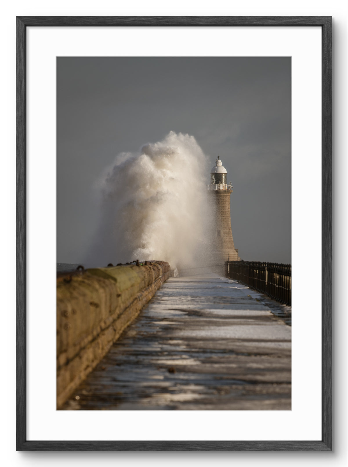Lighthouse on a pier with large waves crashing against it, framed in black.