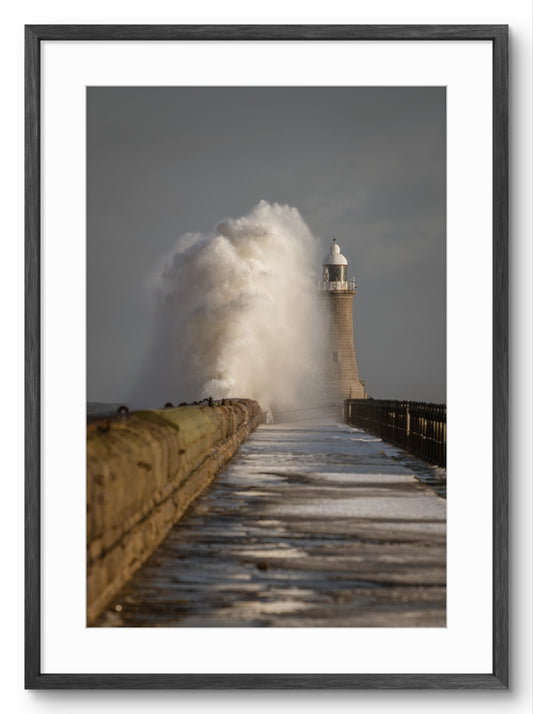 Lighthouse on a pier with large waves crashing against it, framed in black.