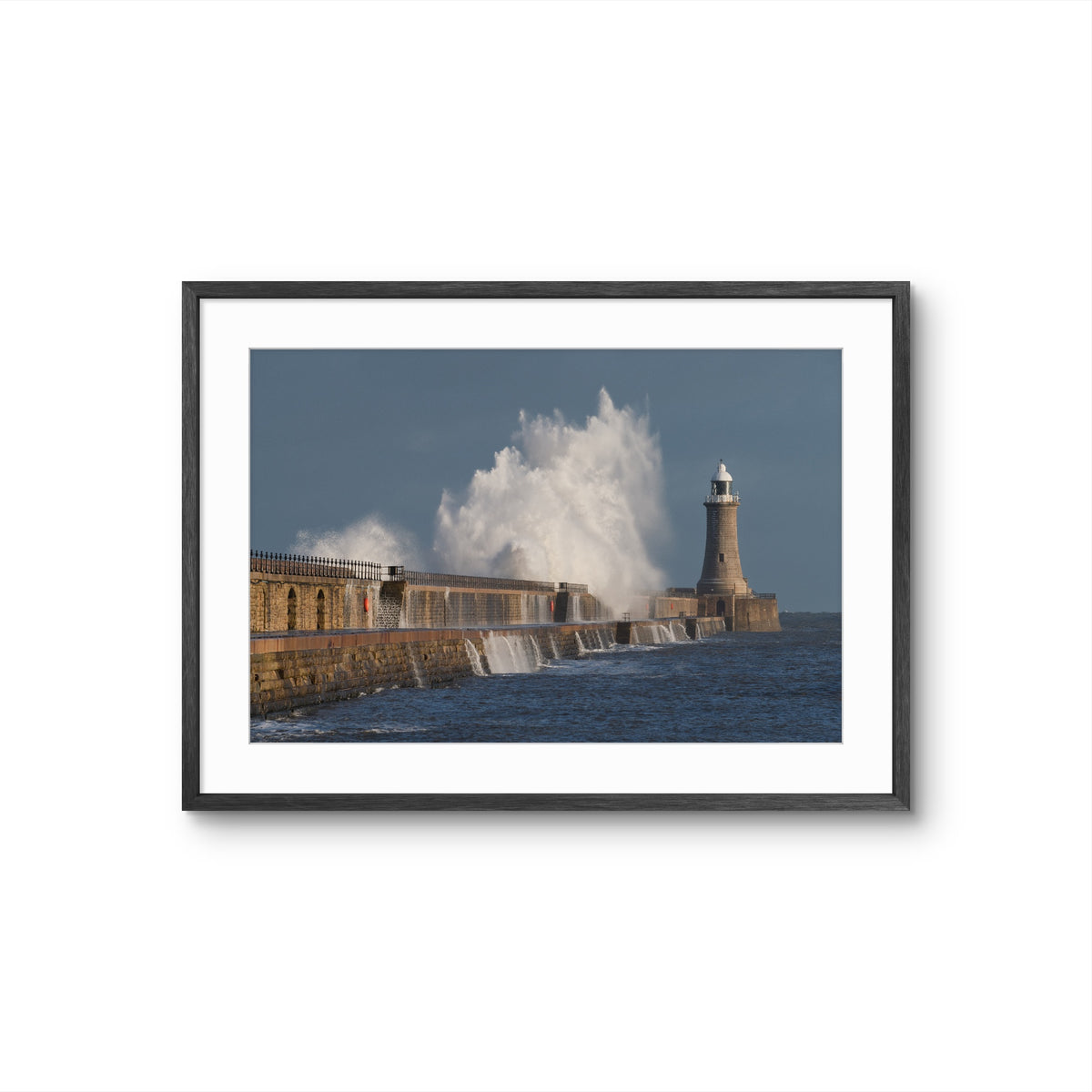 Framed photograph of a lighthouse with large waves crashing against it.