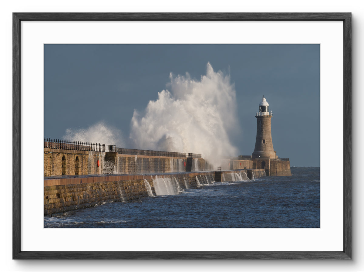 Lighthouse with large waves crashing against a sea wall on a clear day