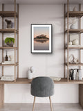 Framed artwork of a castle on a lake in a modern room with shelves and a chair.
