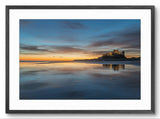 Framed photograph of a castle on a beach at sunset with a blue sky and water reflection.