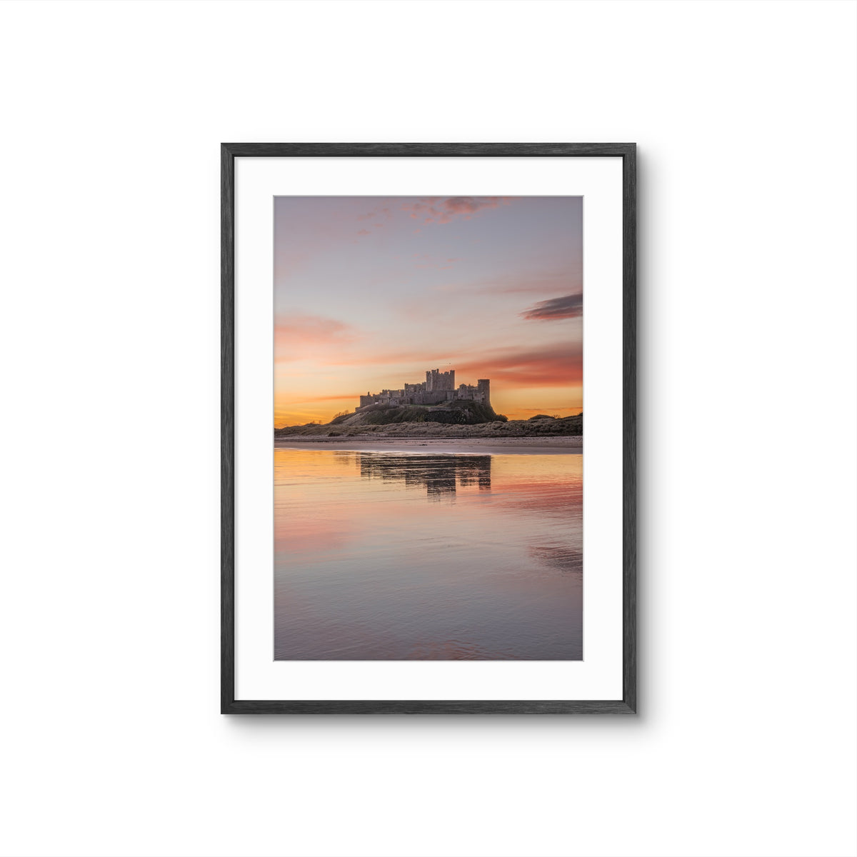 Portrait photograph of Bamburgh Castle at sunrise reflecting in wet sand with soft gold, pink and blue sky tones, Northumberland coast
