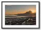 Sunset over a coastal landscape with a castle on a hill, framed in black.