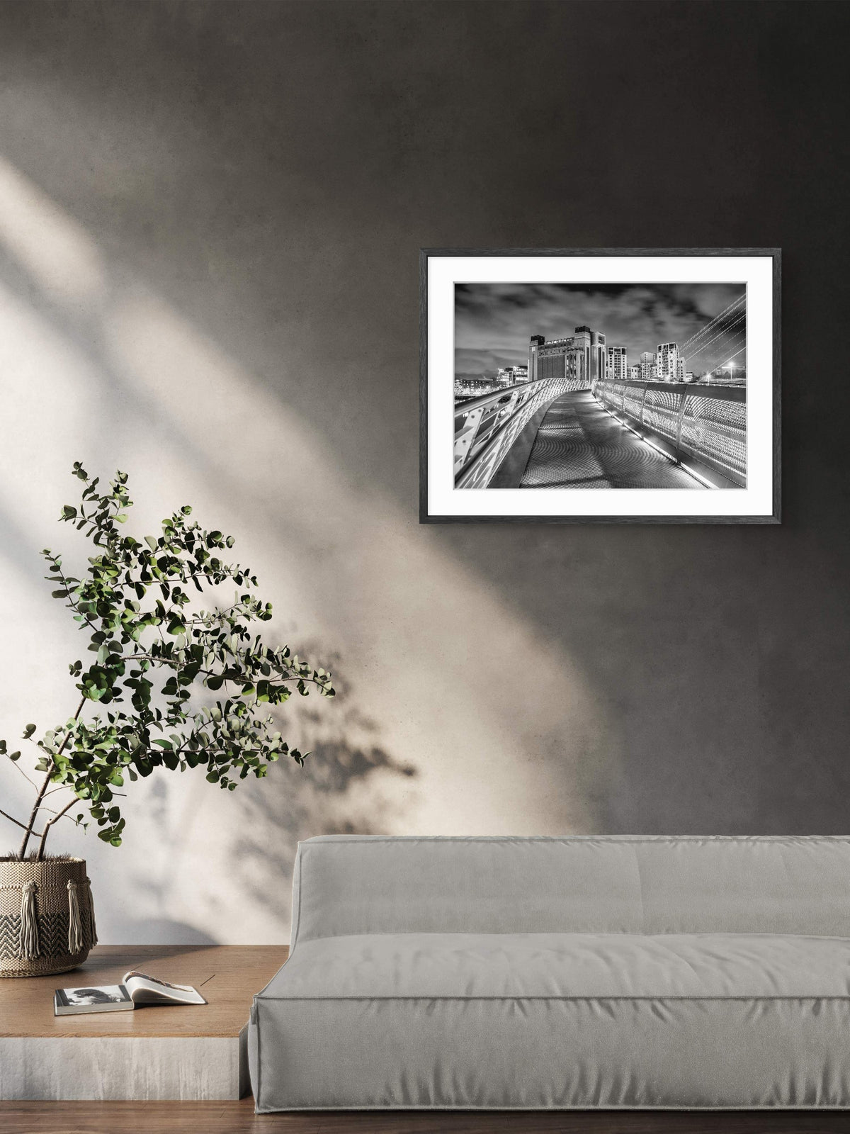 Framed black and white photo of a cityscape on a gray wall above a sofa with a plant.