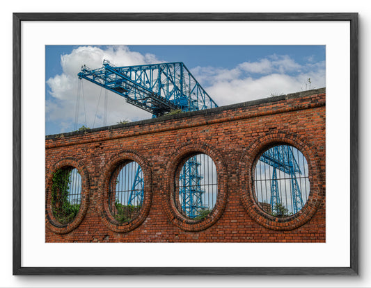 Blue crane reflected in a brick building with arched windows against a blue sky.