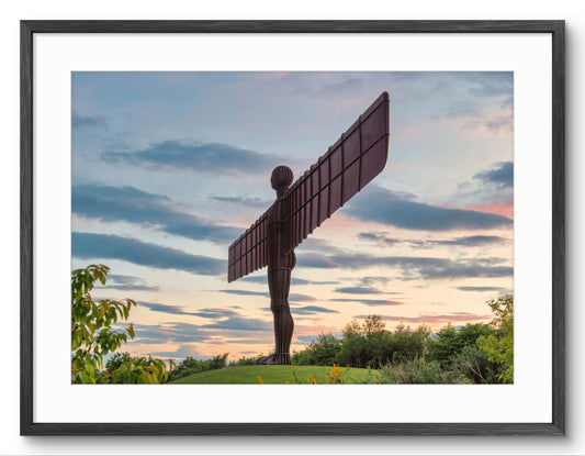 Framed wall art featuring the Angel in the Sky sculpture at sunset, shown with a white mat and a black frame against a white background.