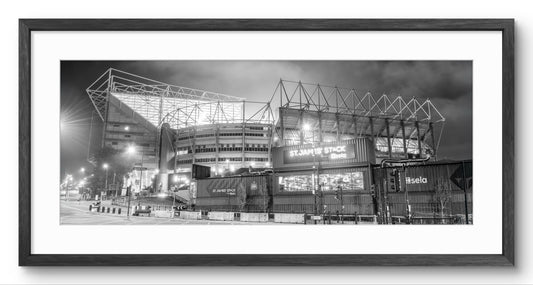 A black and white framed photograph of St James' Park stadium at night, featuring the stadium lights and structure against a dark sky, presented in a black frame with a white mat.